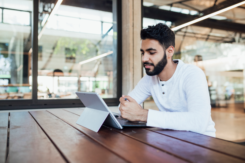 Young man sitting at a table using an electronic tablet.